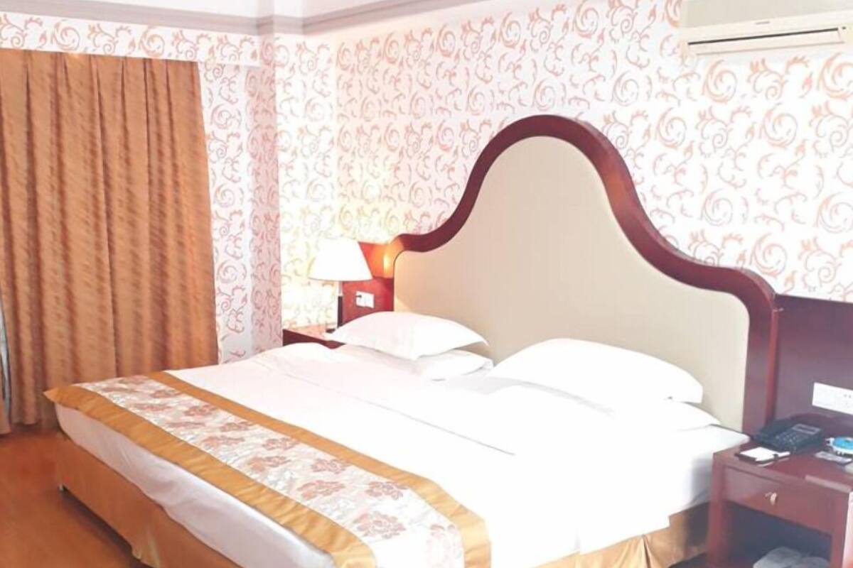 Une chambre d’hôtel avec un grand lit, une table de chevet, un appareil de climatisation et un rideau.