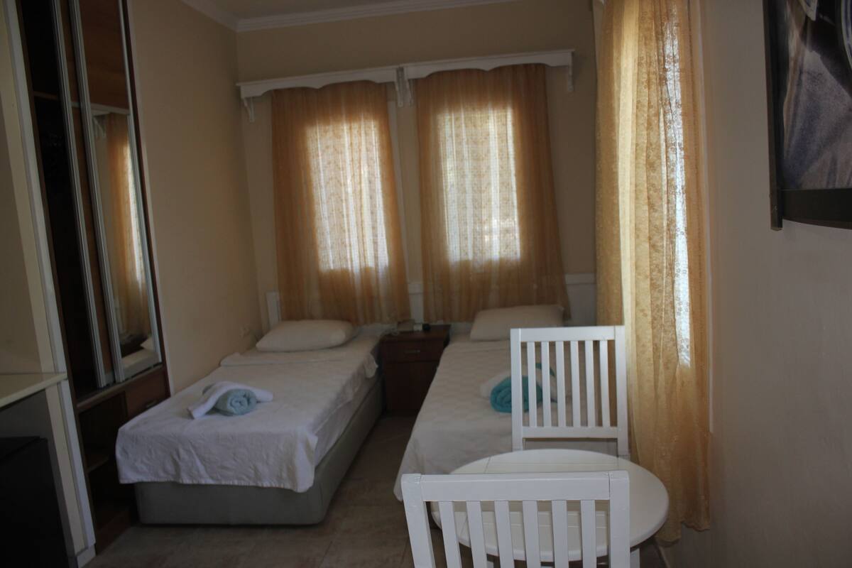 A hotel room with two single beds, a small table, and a chair.
