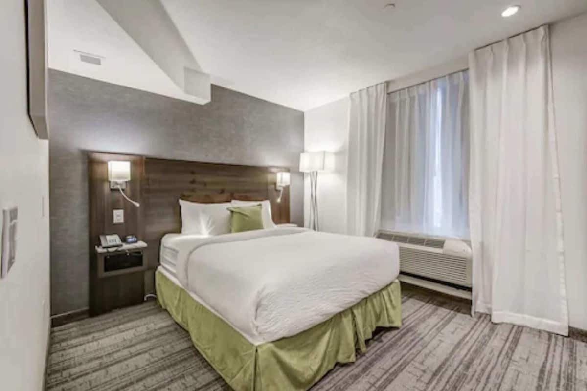 A hotel room with a large bed, bedside lamps, a telephone, a nightstand, and a window with curtains.