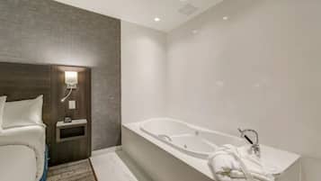 Un baño moderno con una bañera grande, un lavamanos blanco y una mesita de noche con una lámpara.