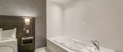 Un baño moderno con una bañera grande, un lavamanos blanco y una mesita de noche con una lámpara.