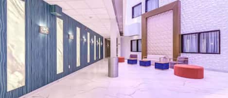 A hotel lobby with a marble floor, blue and white textured walls, and a seating area with colorful ottomans.