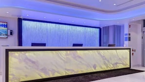 Un mostrador de recepción moderno con superficie similar al mármol, alfombra oscura y pared iluminada en azul.