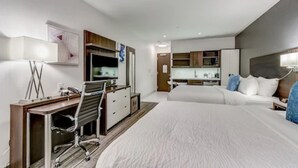 Una habitación de hotel moderna con una cama grande, un escritorio con silla, kitchenette y baño.