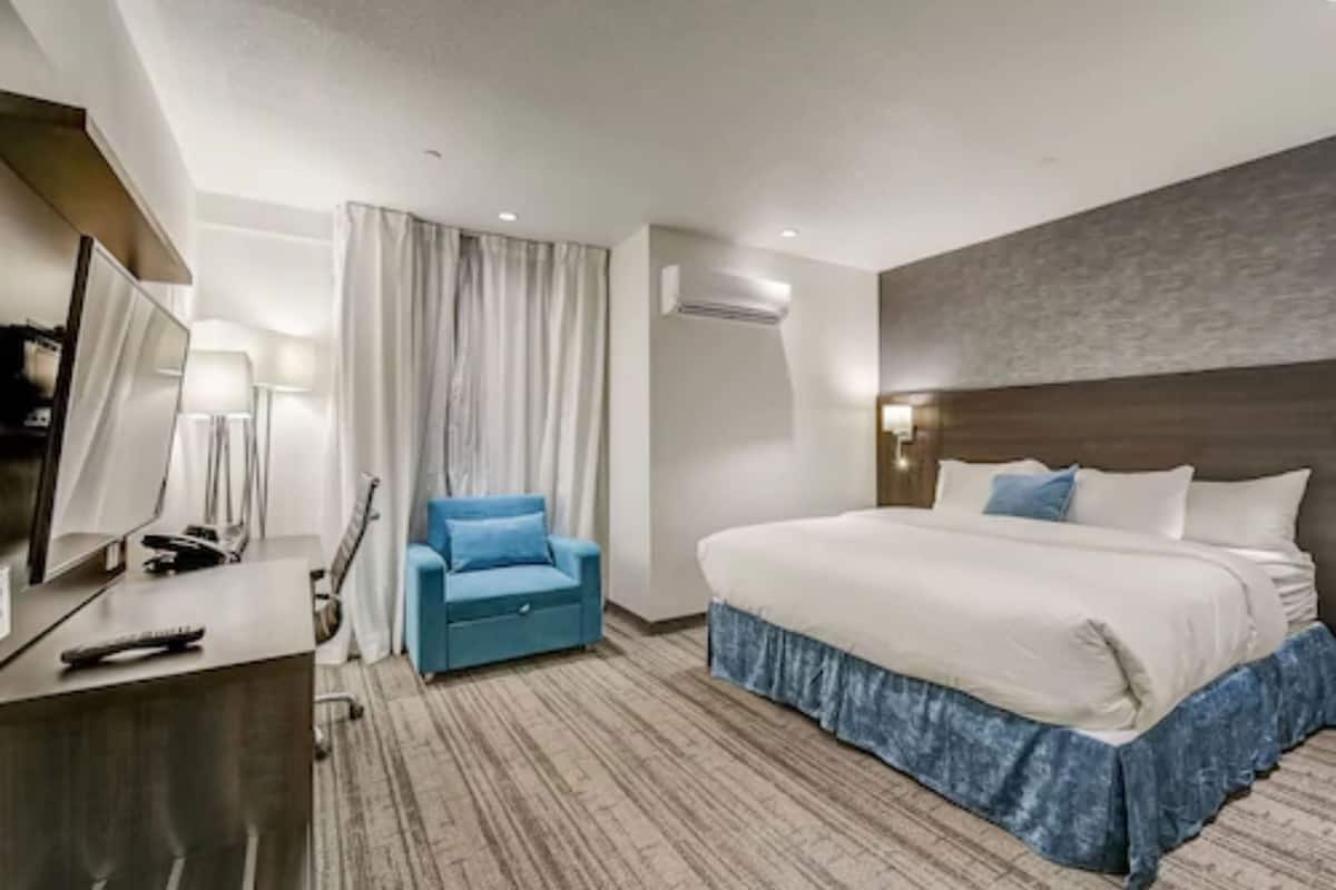 A hotel room with a bed, a desk with a computer, a chair, and a TV.