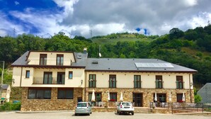Un edificio de dos pisos con fachada de piedra, varios balcones y paneles solares en el techo.