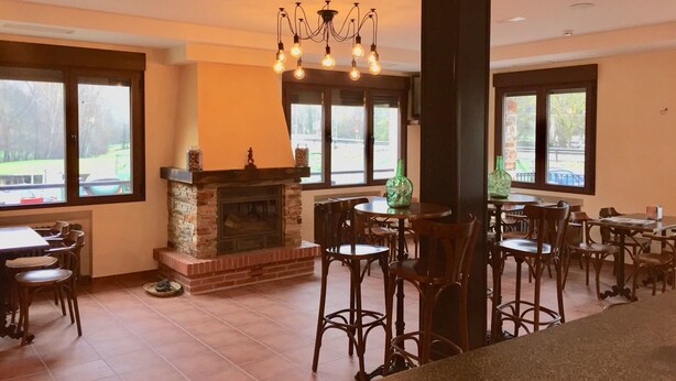Un comedor espacioso con chimenea de piedra, varias mesas y sillas, y grandes ventanales con vistas al exterior.