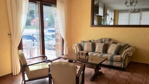 Una sala de estar con un sofá, dos sillones, una mesa de centro y un ventanal con cortinas.