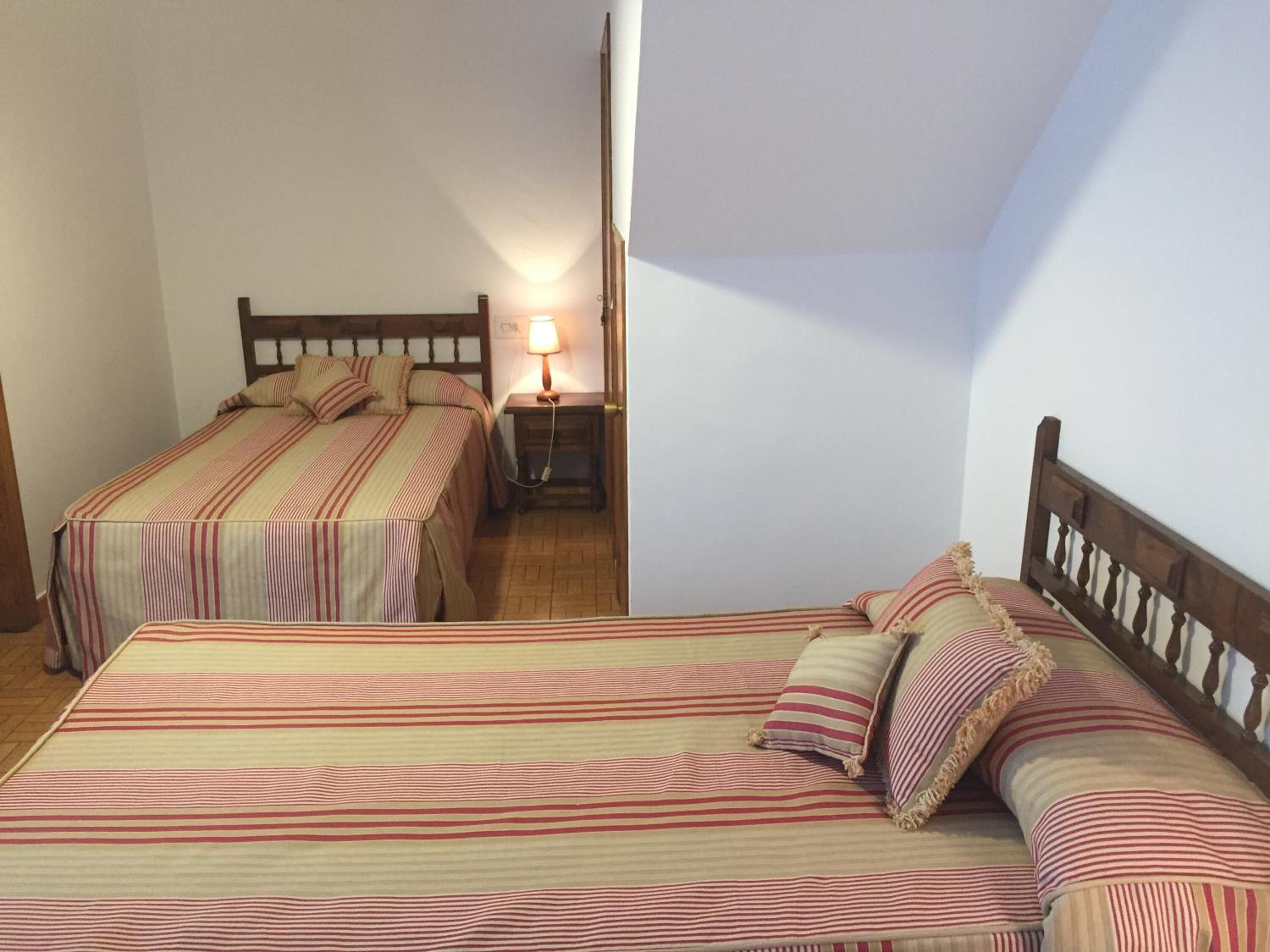 A room with two beds, each with striped bedding and wooden headboards. There is a nightstand with a lamp between the beds.