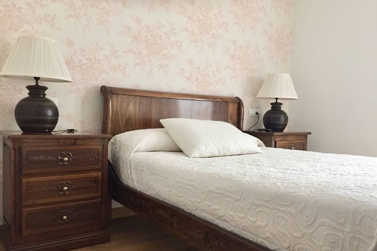 A bedroom with a wooden bed, two nightstands, a dresser, and floral wallpaper.