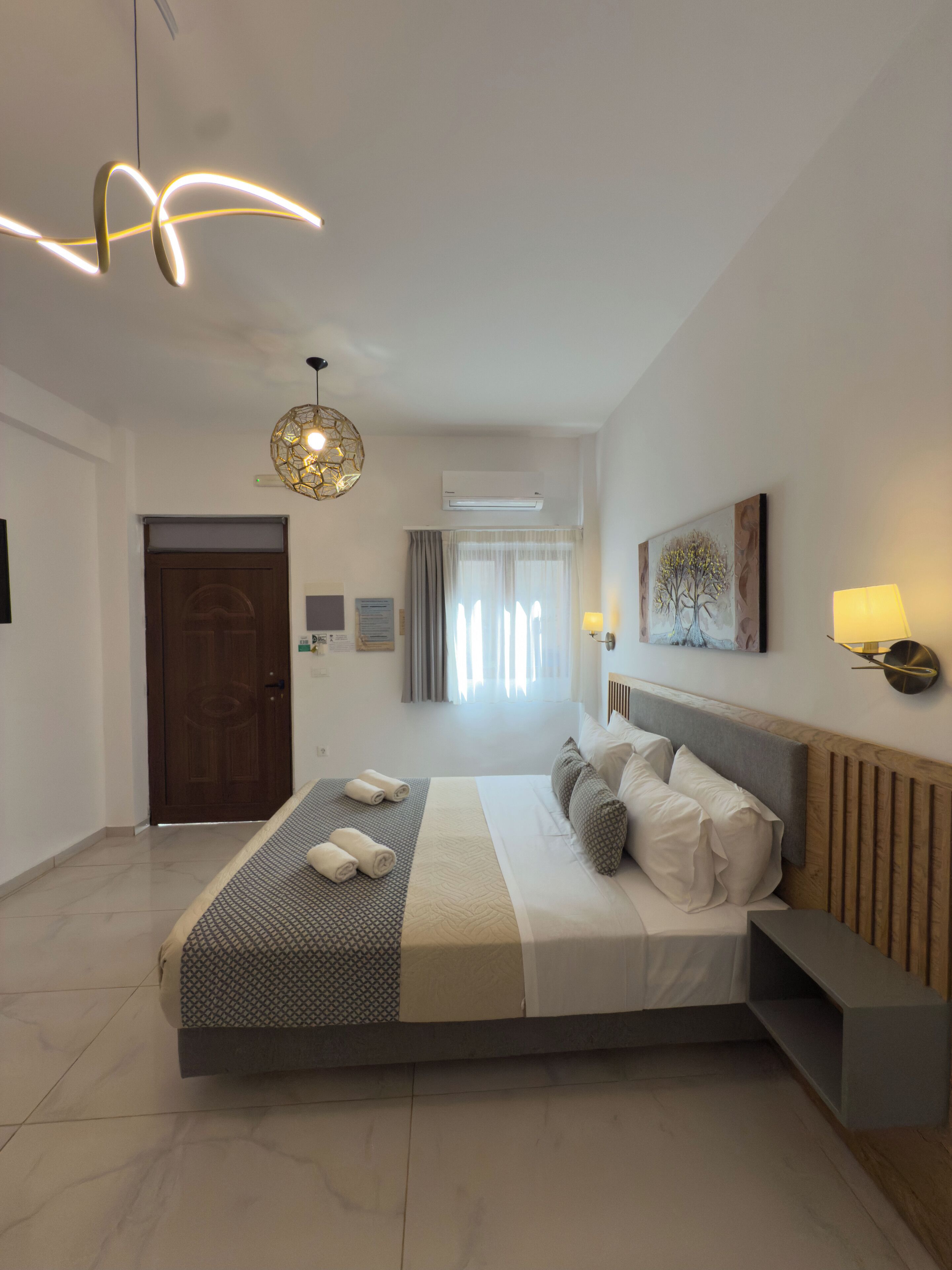 A modern bedroom with a large bed, a wooden headboard, a bedside table, and a hanging light fixture.
