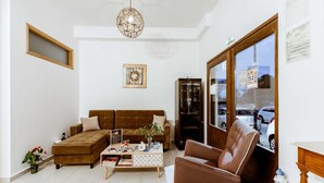 A modern living room with a brown sofa, a coffee table, and a brown armchair. There is a cabinet with glass doors and a framed picture on the wall. - Deluxe Suites (Chania)