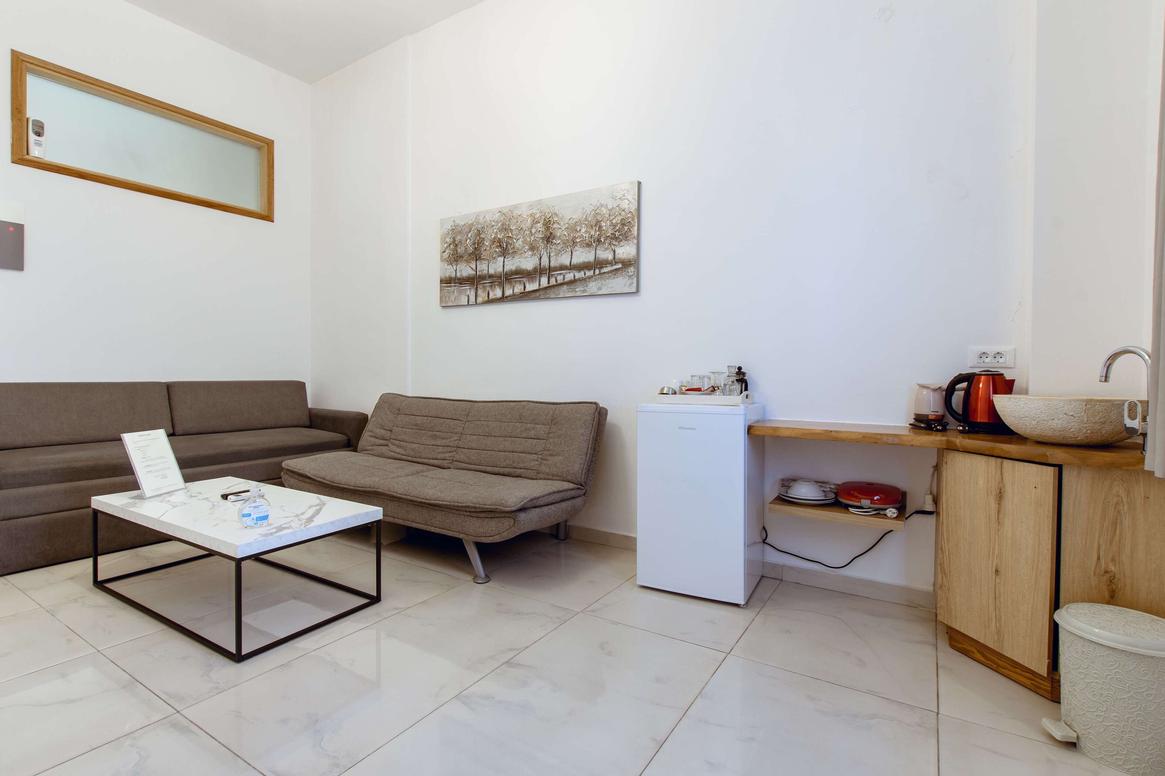 Un espace de vie compact comprenant un canapé, une table basse, un petit réfrigérateur, un meuble en bois et un tableau accroché au mur.