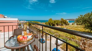 A balcony with a table set with fruits, overlooking a coastal area with a clear sky. - Deluxe Suites (Chania)