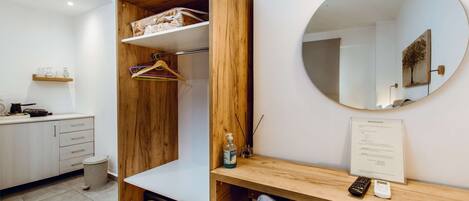 A modern room with a wooden wardrobe, a desk with a mirror, and a small trash bin.
