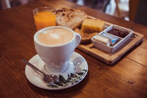 A cup of coffee on a saucer with a spoon, a glass of orange juice, toast, butter, jam, and a small dish of honey on a wooden table.