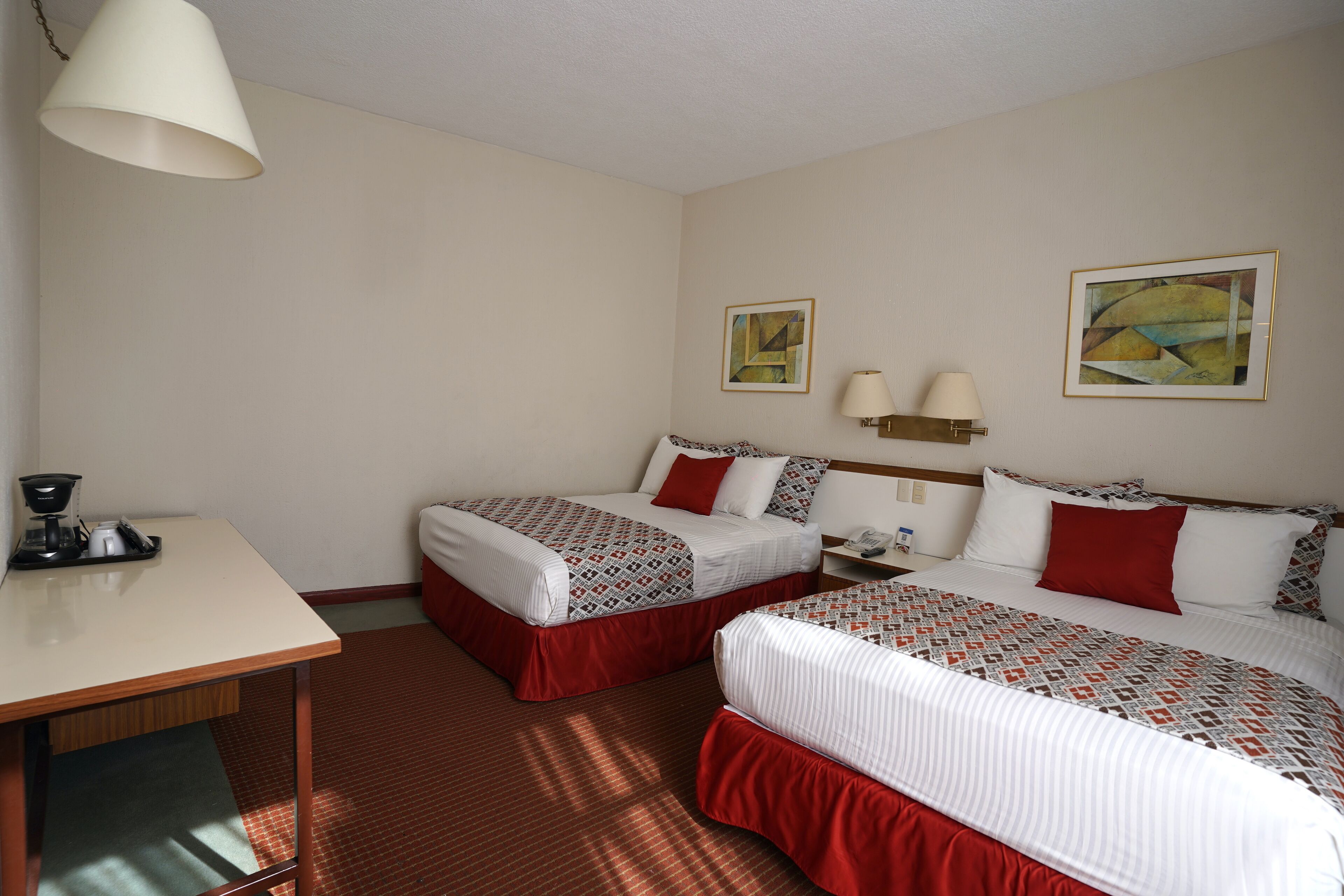 Quarto de hotel com duas camas, uma escrivaninha e uma cafeteira.