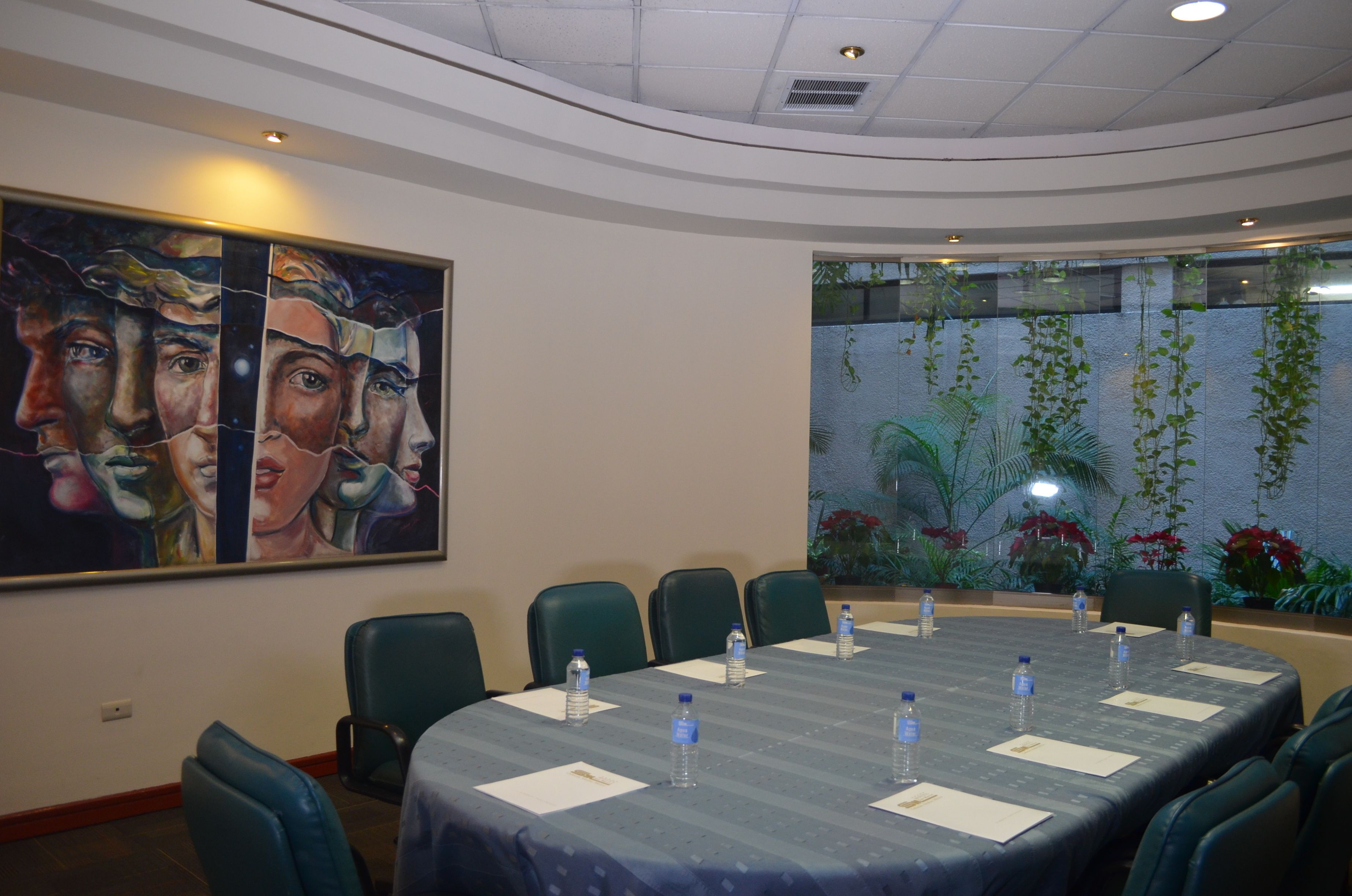 Un salón de conferencias con una larga mesa, sillas, botellas de agua y un cuadro grande en la pared.
