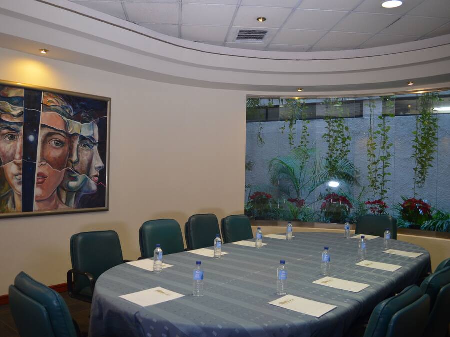 Une salle de conférence avec une longue table, des chaises, des bouteilles d’eau et un grand tableau accroché au mur.