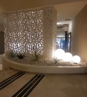Een hal met een decoratieve witte scheiding, een grindvloer en een rond zitgedeelte met verlichting.