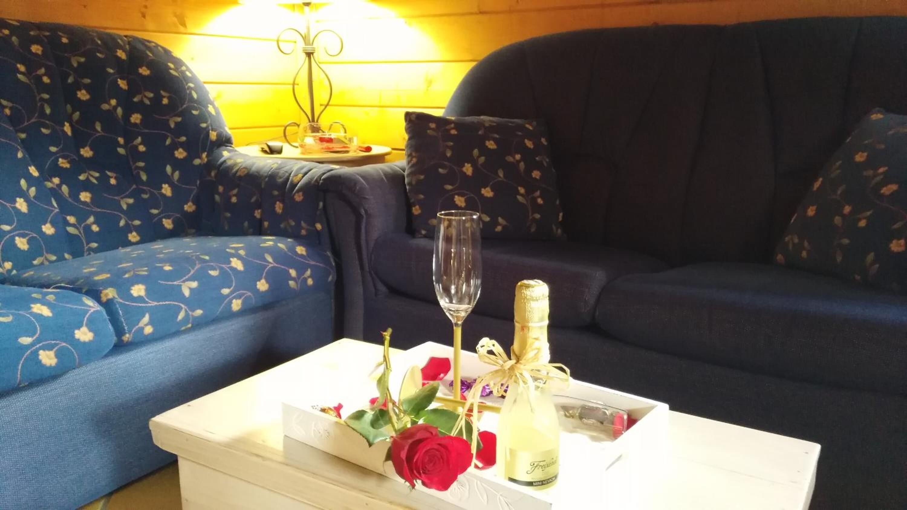 Een kamer met een blauwe bank en een witte salontafel met een champagnefles, een glas en een rode roos.