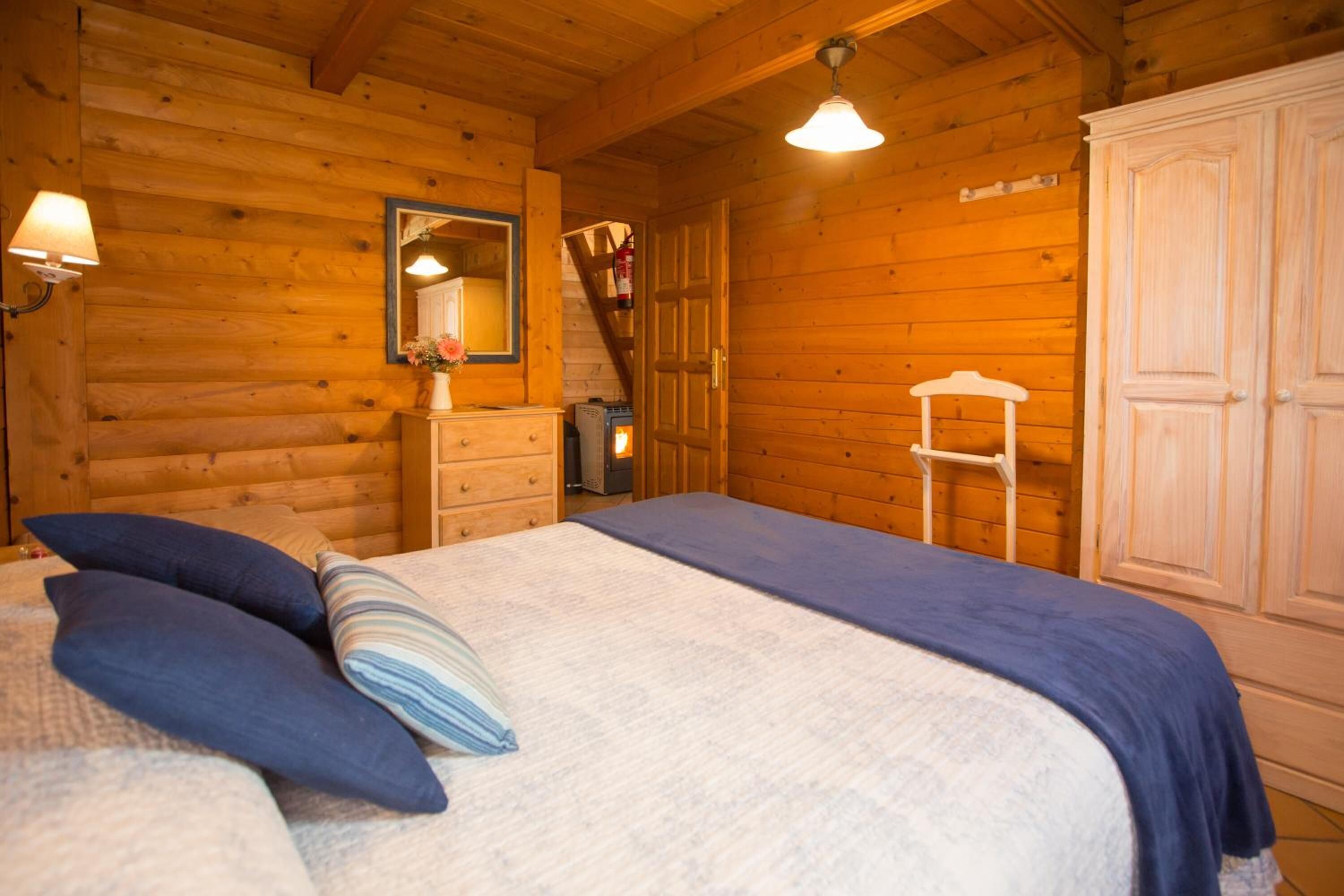 A wooden cabin bedroom with a bed, dresser, mirror, and wardrobe.