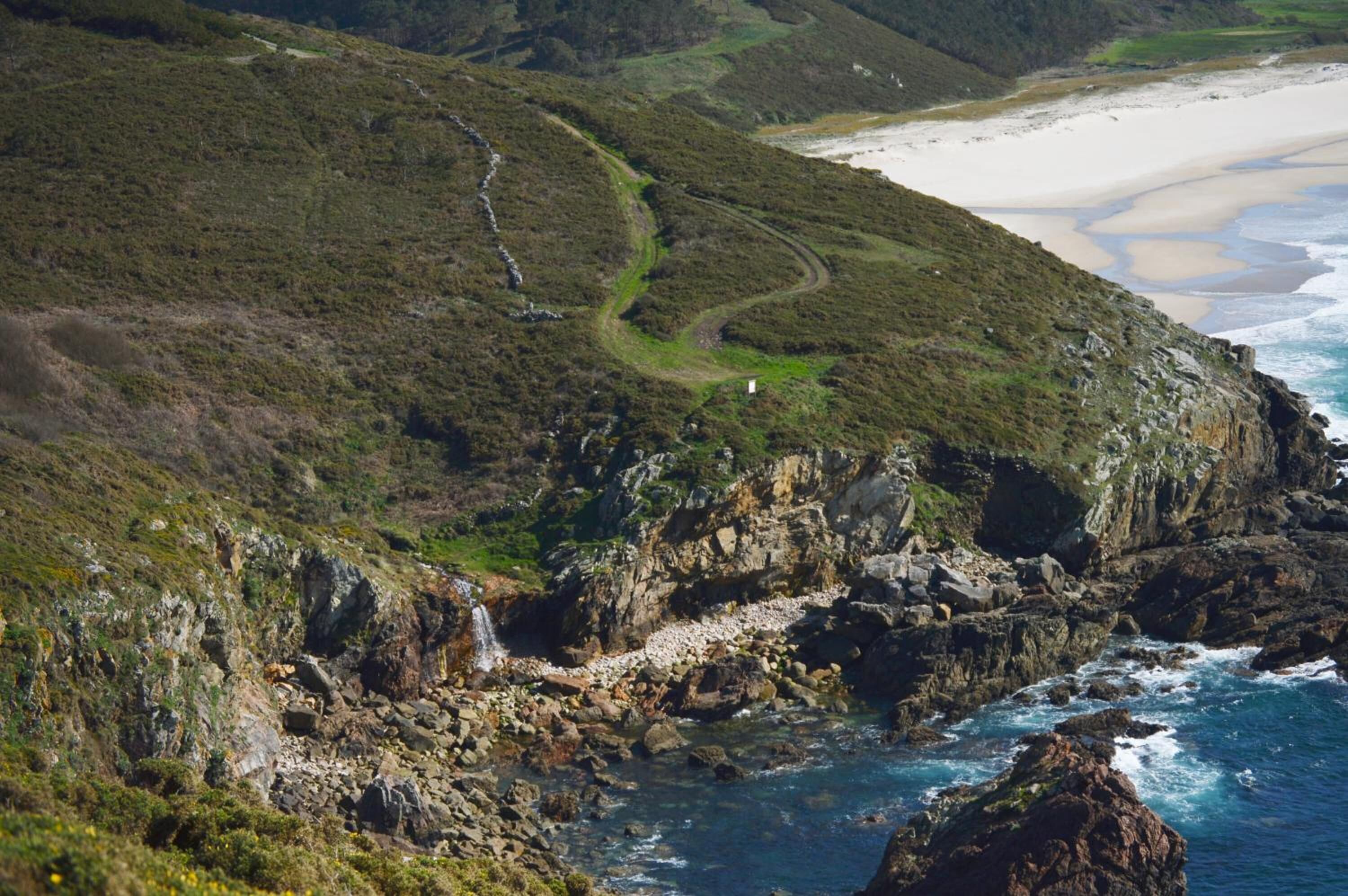 A coastal landscape with a winding path, rocky cliffs, and a beach.