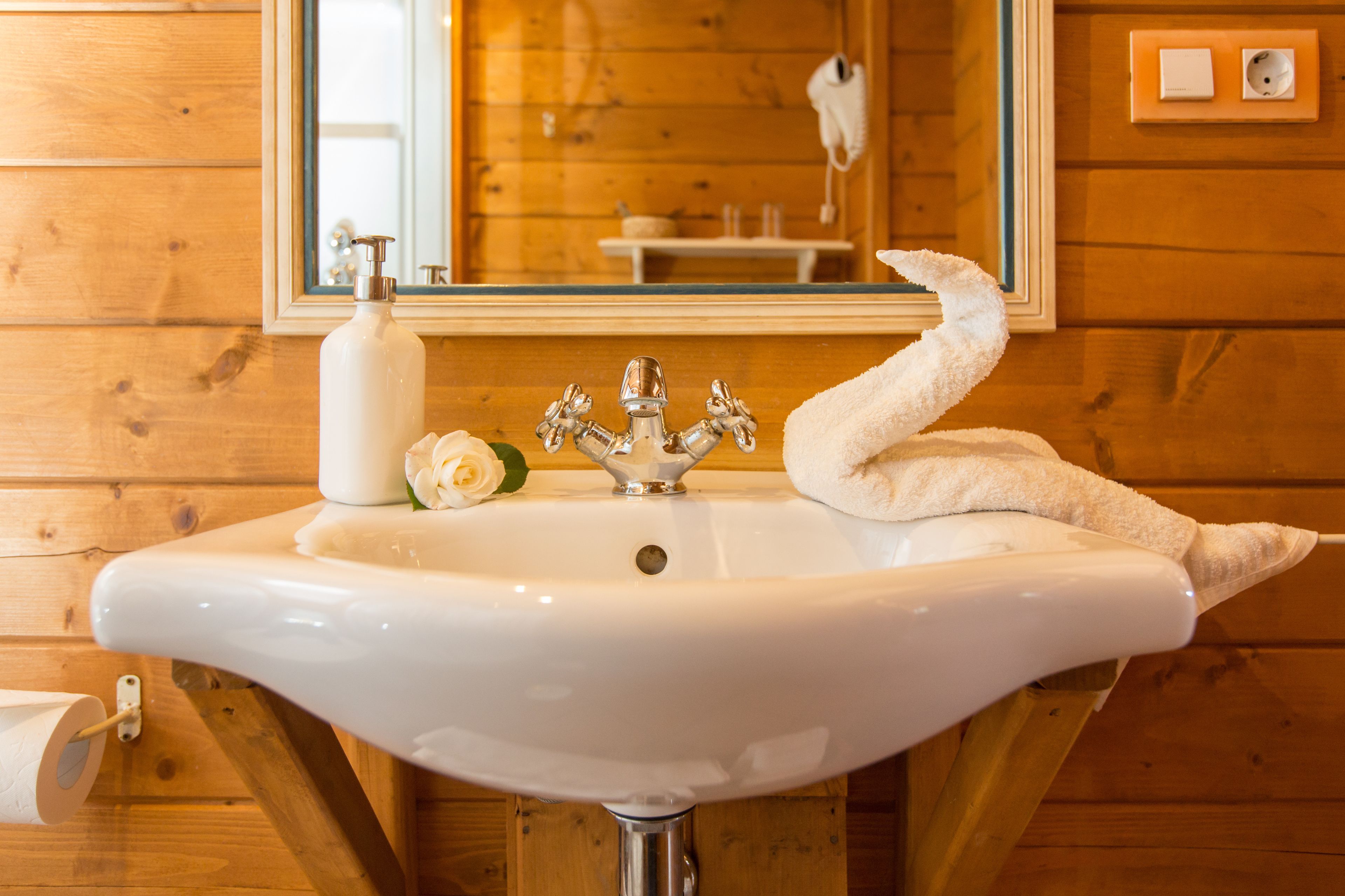 A white bathroom sink with a mirror above it, wooden walls, and a towel hanging on the right side.