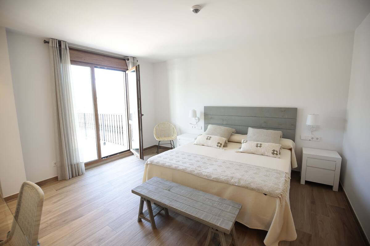 Ein Schlafzimmer mit Bett, Bank, Nachttisch und Blick ins Freie.