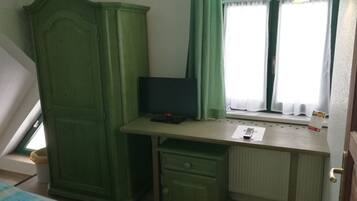 A bedroom with a bed, a desk with a computer, a wardrobe, and a window with curtains.