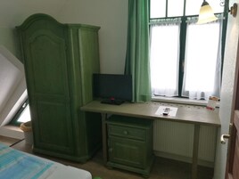 A bedroom with a bed, a desk with a computer, a wardrobe, and a window with curtains.