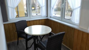 A corner room with a round table and two chairs, wooden walls, and large windows with curtains. - Hotel Villa Alice (Thale)