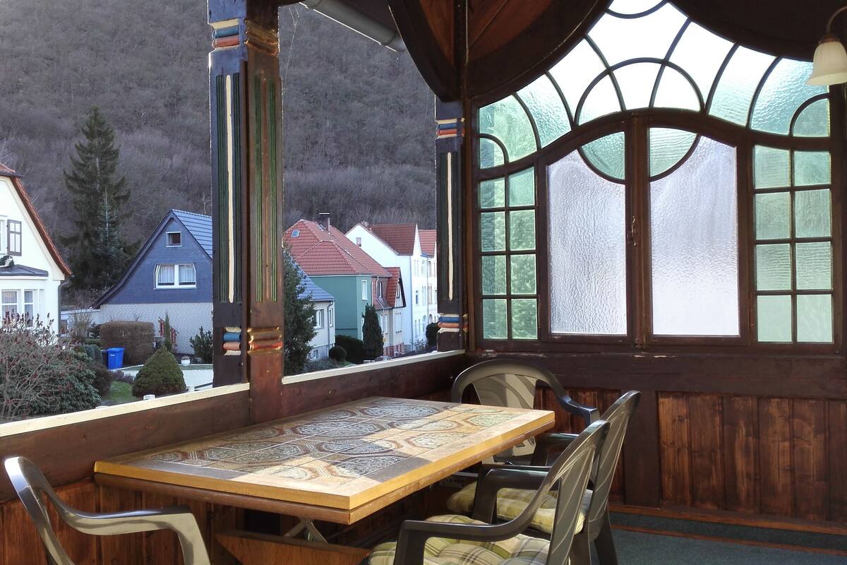 A wooden table with chairs in a room with large windows.