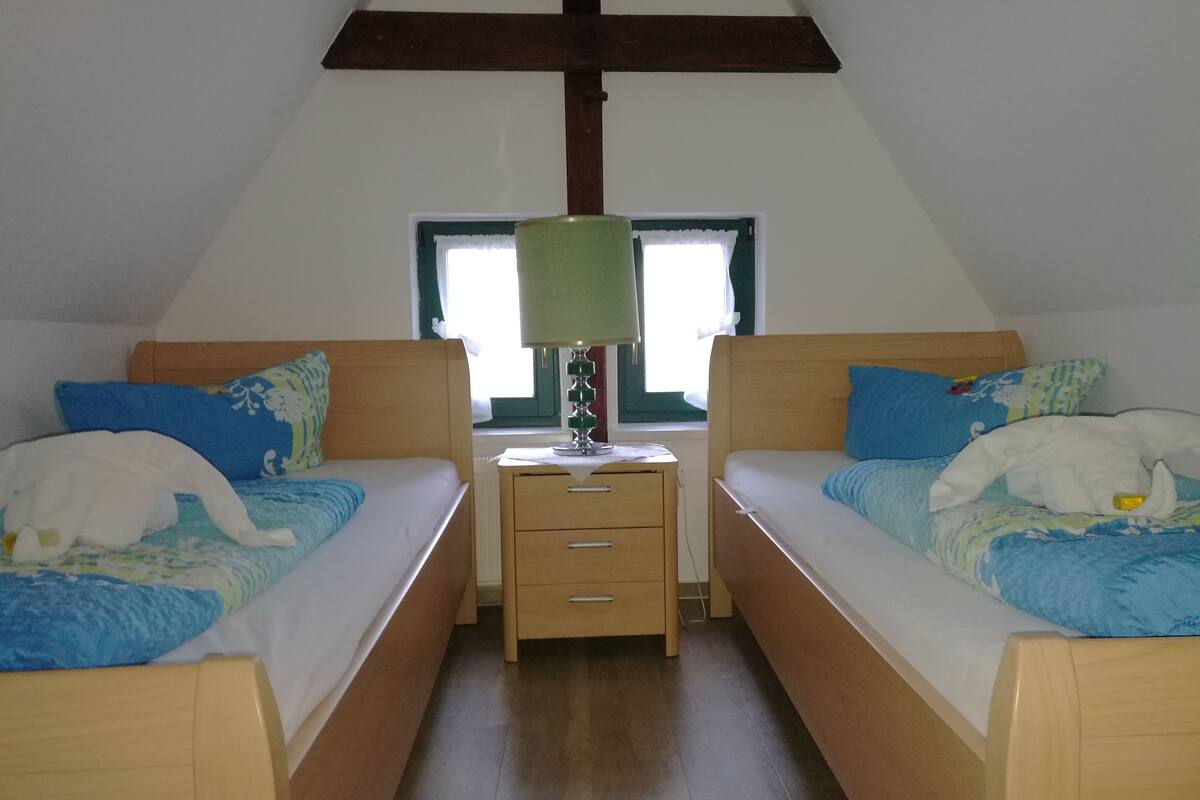 A bedroom with two beds, a nightstand, and a window with curtains.