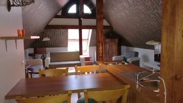 A cozy attic-style room with a wooden dining table, chairs, and a built-in sink.