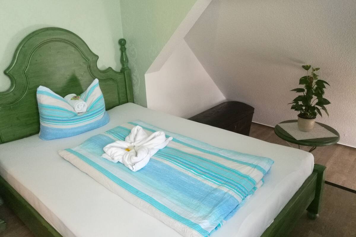 A neatly made bed with striped bedding, a green headboard, and a small bedside table with a plant.