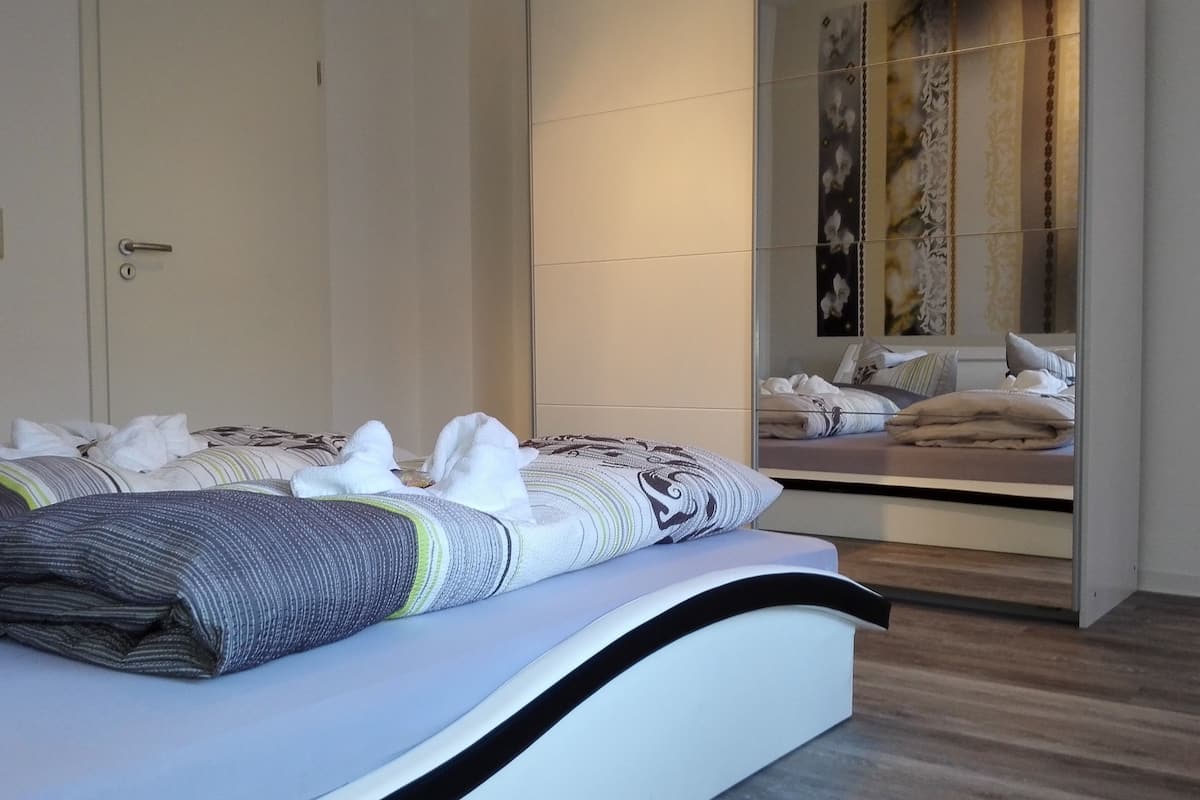 A modern bedroom with a large bed, a bedside table, and a mirror.