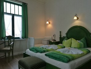 A bedroom with a green headboard, a white mattress, green and white bedding, a wooden chair, a nightstand with a lamp, and a window with green curtains. - Hotel Villa Alice (Thale)