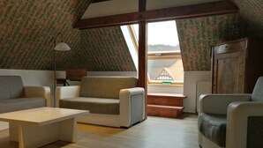 A cozy loft-style living room with a sofa, armchairs, and a coffee table. A window provides a view of a house and a door labeled "Notausstieg". - Hotel Villa Alice (Thale)