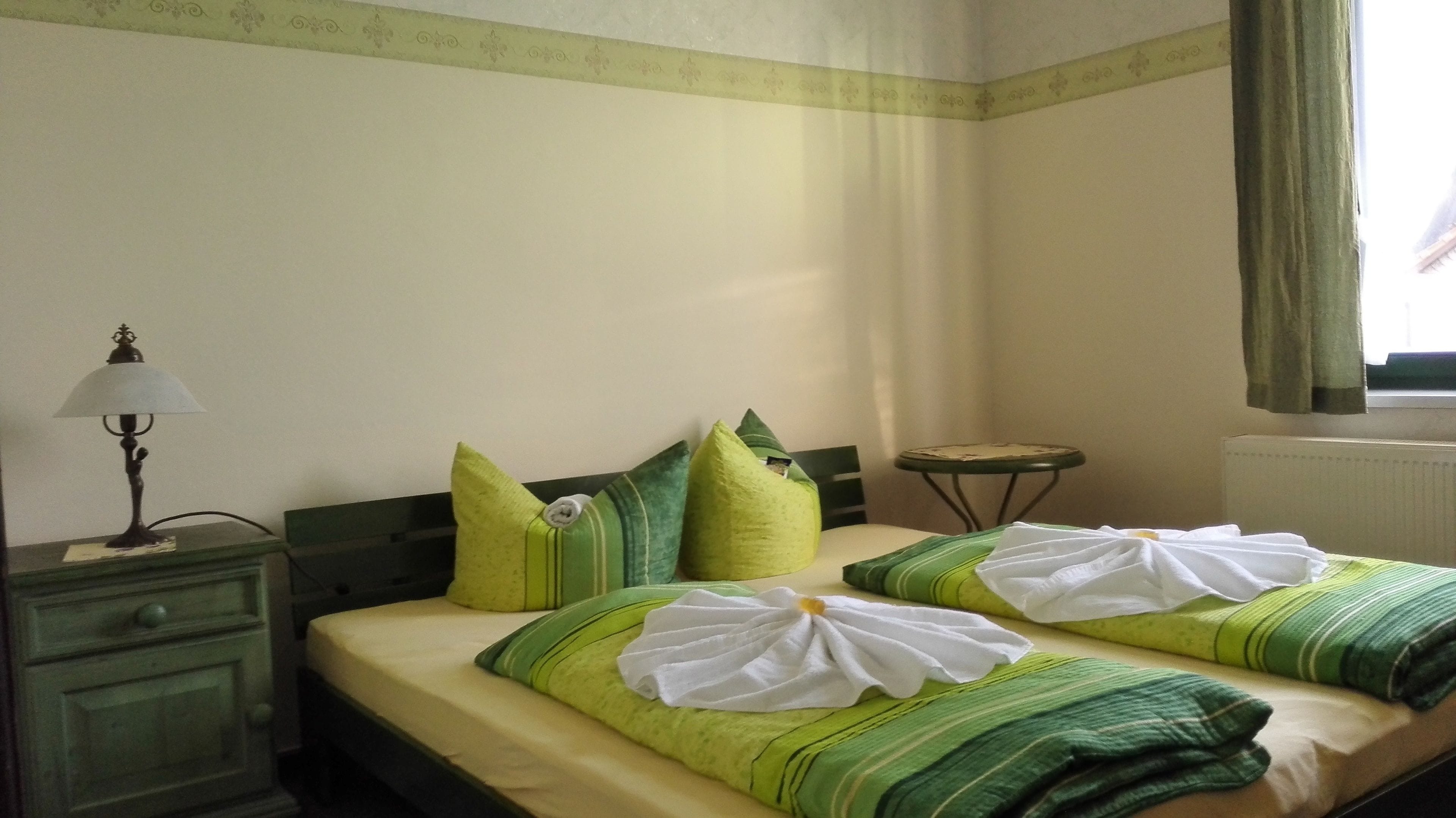 A hotel room with two beds, a small table, a lamp, and a window with curtains.