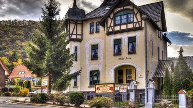 A traditional building with a central tower, a signboard, and a well-maintained garden. - Hotel Villa Alice (Thale)