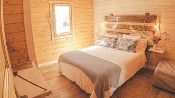 A cozy bedroom with a wooden ceiling, a bed with a headboard, a window, and a bedside table.