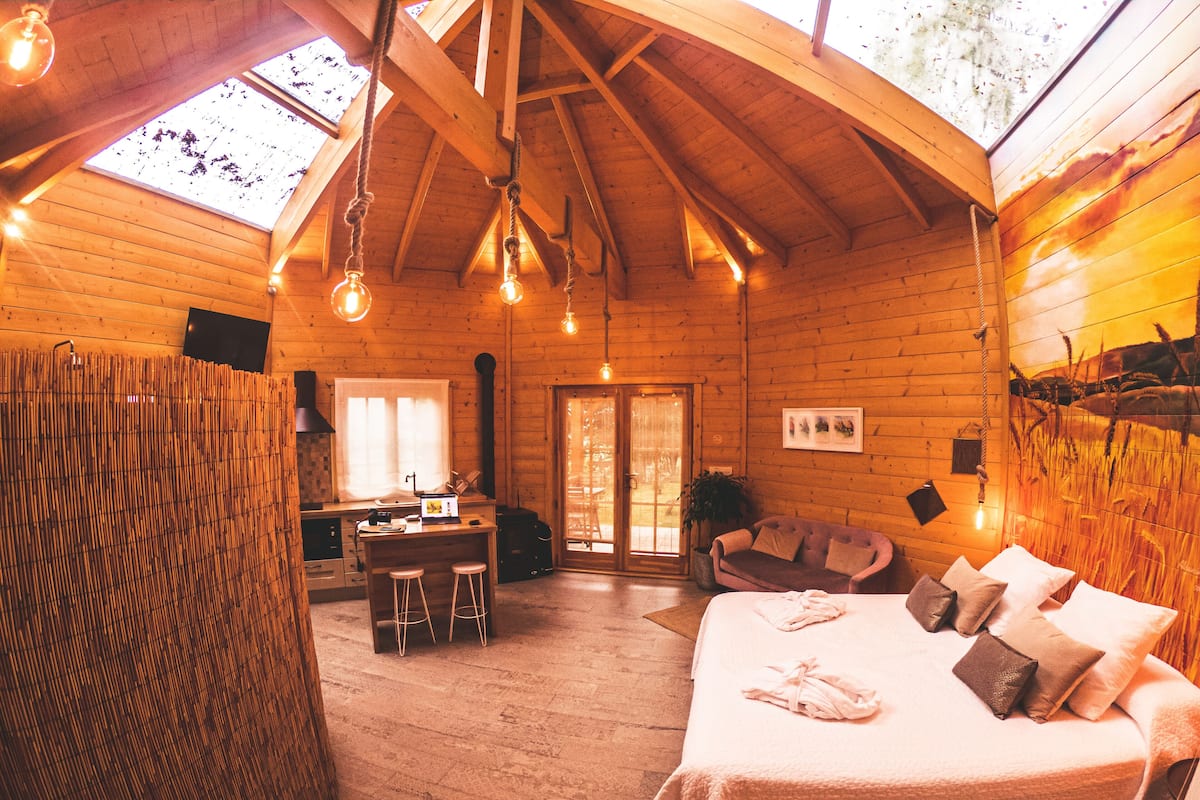 A cozy log cabin with a large bed, a dining area, and a view of the outdoors through skylights.