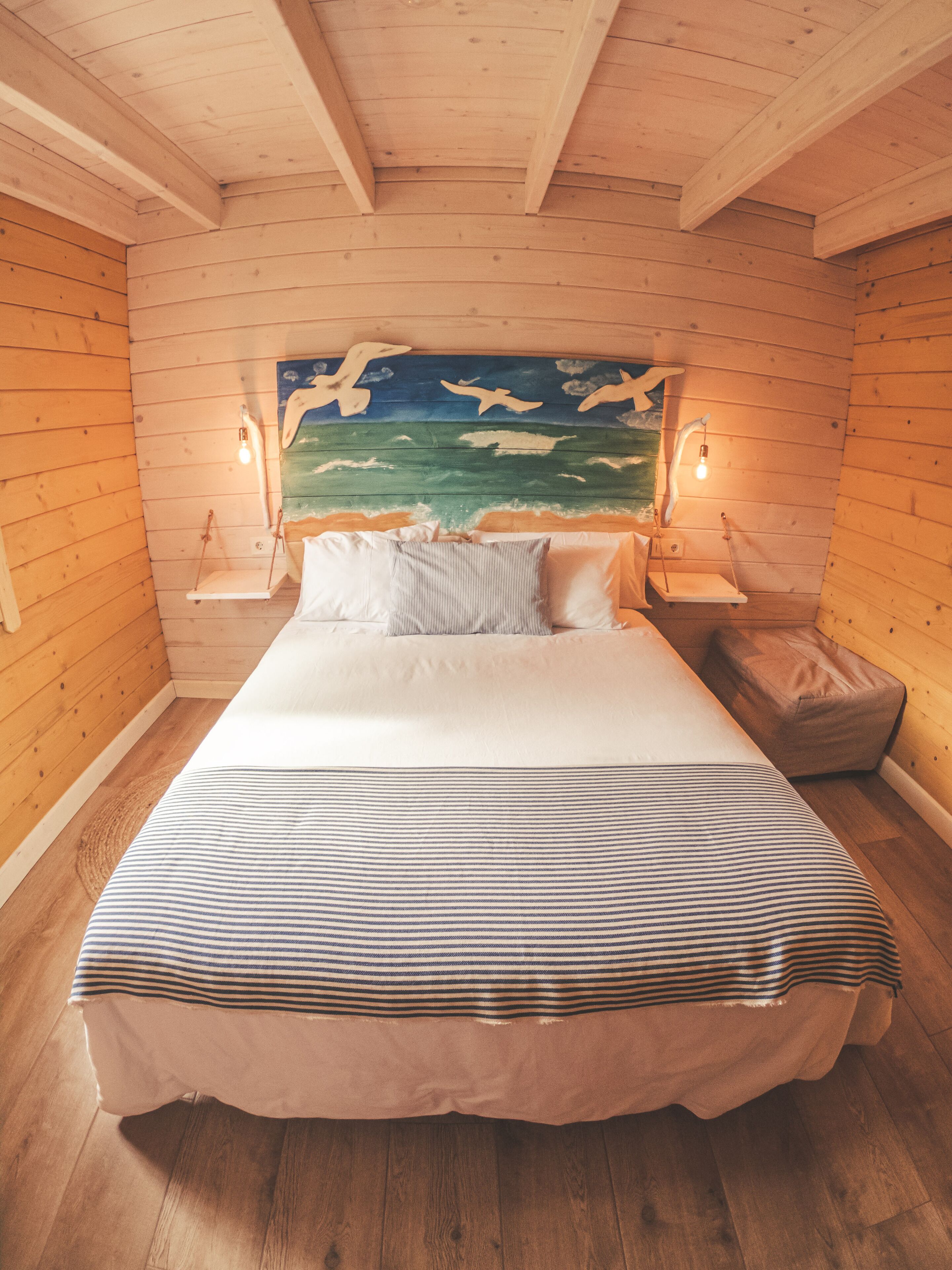 A bedroom with a large bed, wooden walls, a painted mural of seagulls, and two bedside lamps.