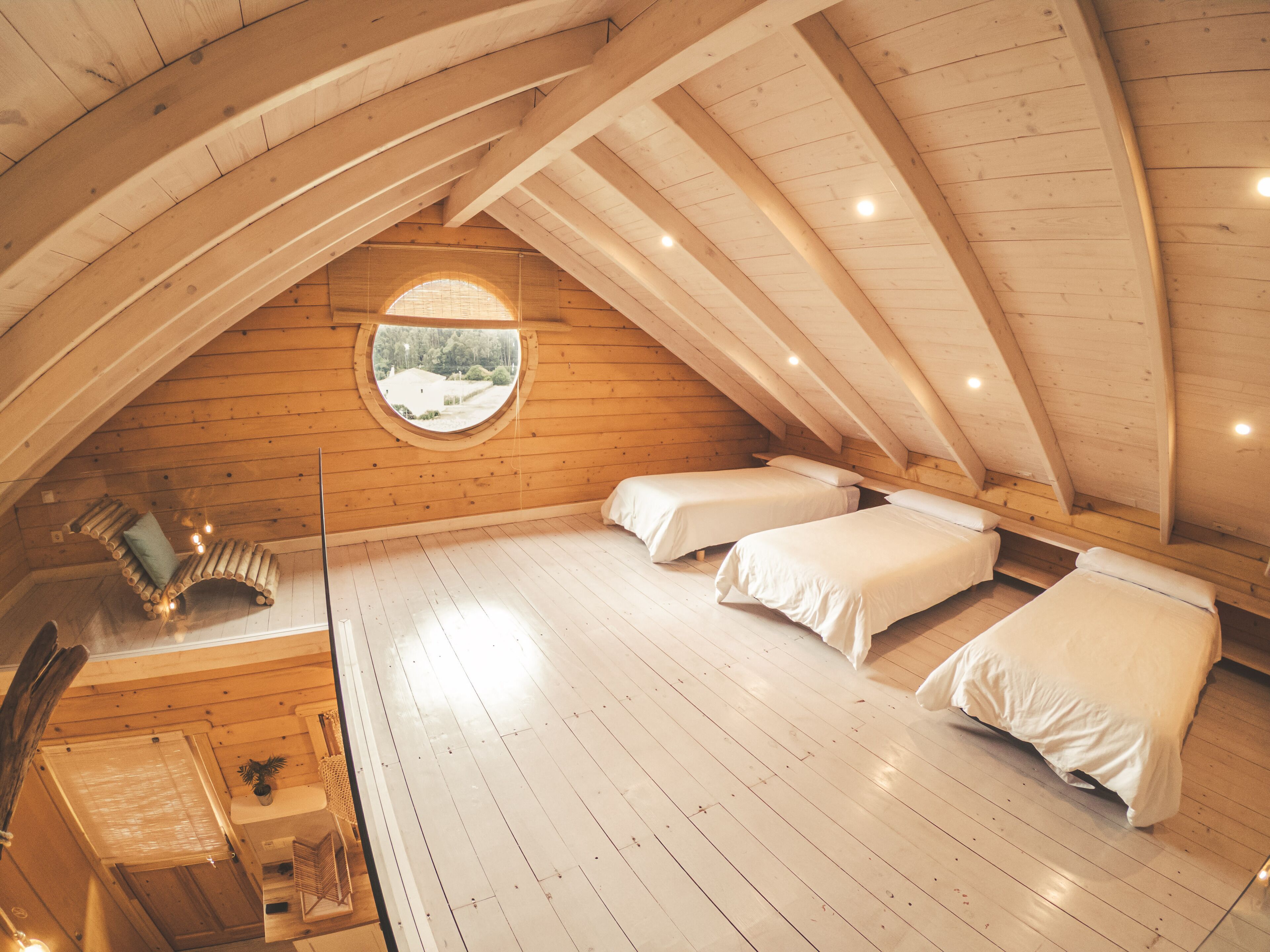 A cozy attic bedroom with wooden beams, a circular skylight, and two beds.