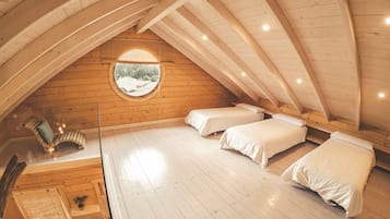 A cozy attic bedroom with wooden beams, a circular skylight, and two beds.