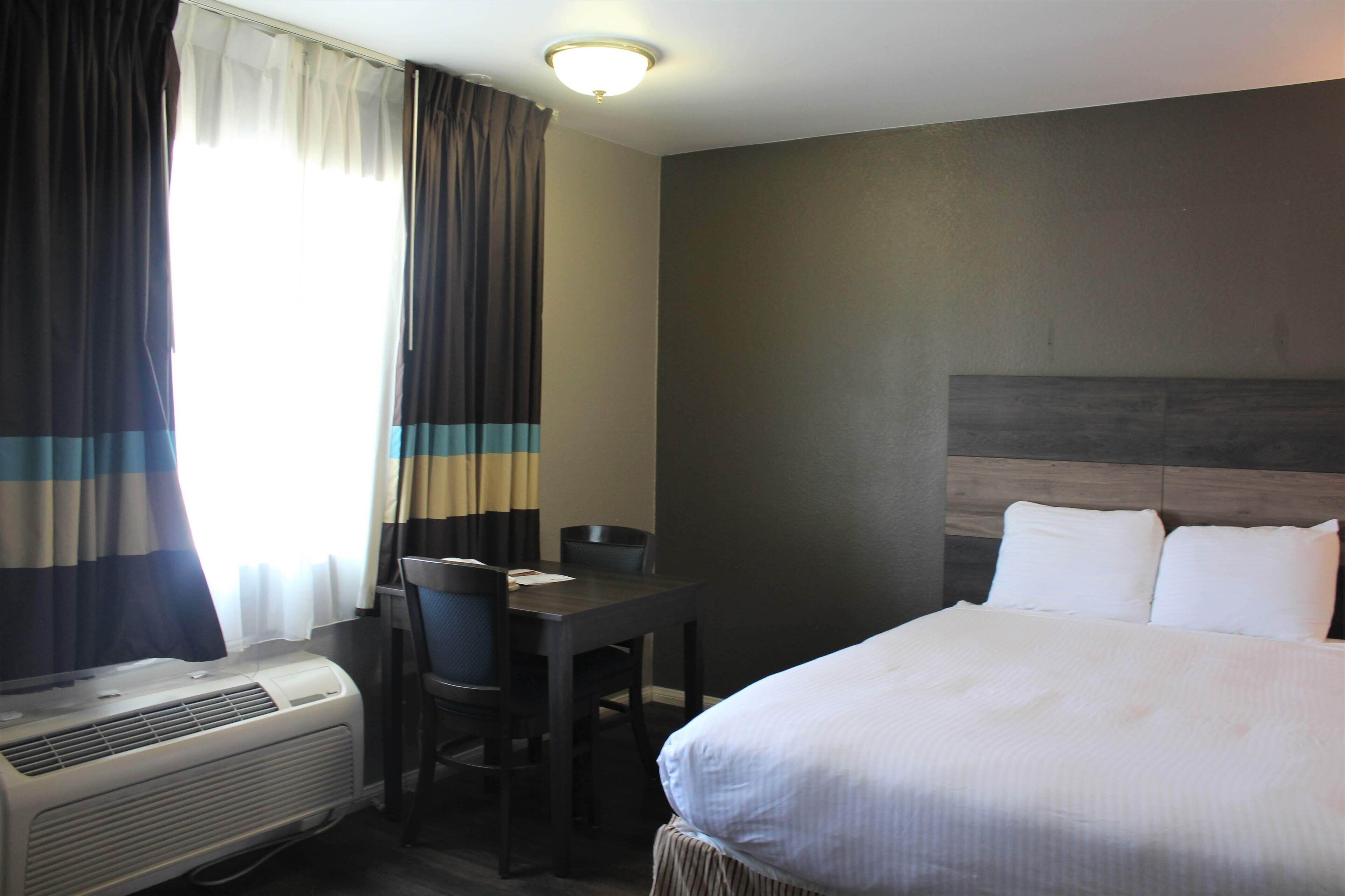 A hotel room with a bed, a desk, a chair, and an air conditioning unit.