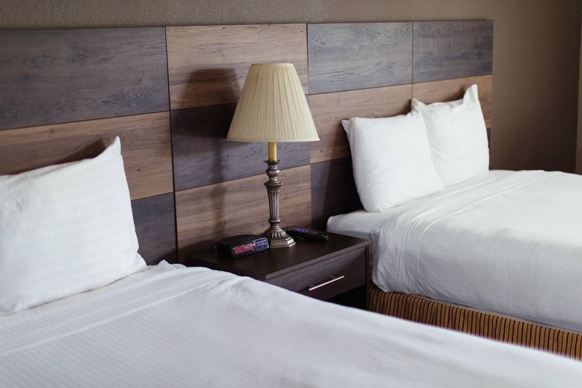 A hotel room with two beds, a nightstand with a lamp, and a remote control.