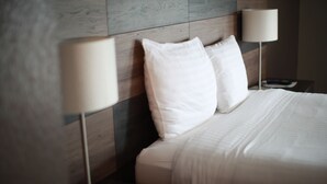 Un lit bien fait, avec du linge de lit blanc et deux lampes de chevet.