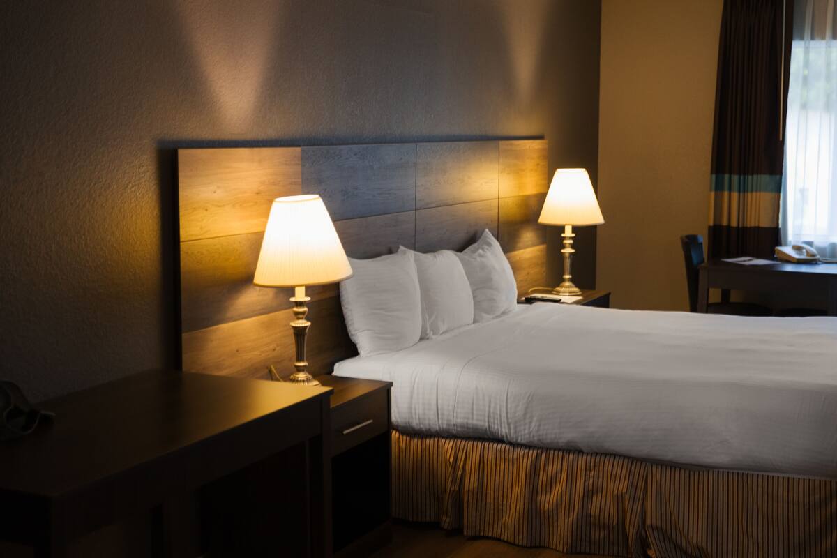 A hotel room with a large bed, two bedside lamps, a wooden headboard, a desk, and a chair.